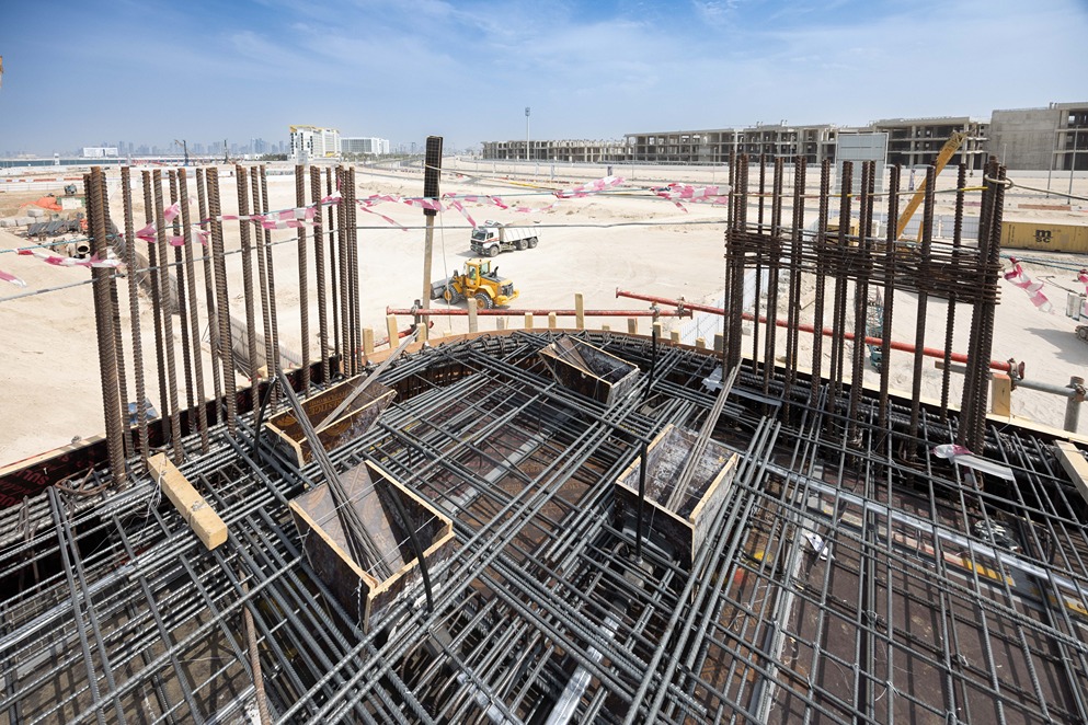 Beach Walk Iii By Imtiaz Construction site showing steel rebar framework and machinery against a backdrop of a clear blue sky.